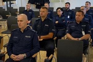 policjanci siedzą na krzesłach, słuchają organizatorów zawodów i przystępują do pisania testu