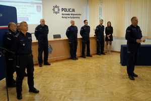 policjanci siedzą na krzesłach, słuchają organizatorów zawodów i przystępują do pisania testu