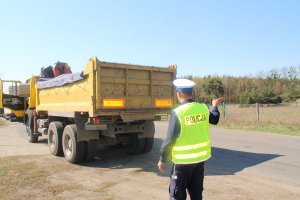 Policjant ruchu drogowego sprawdza prawidłowość działania kierunkowskazów tylnych. Pokazuje ręką w prawą stronę.