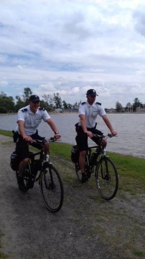 policjanci jadą na rowerach nad brzegiem jeziora