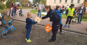 Policjantka wręcza dziewczynce kolorowankę - nagrodę za udział w konkursie.  W tle widoczni są rodzice przedszkolaków.