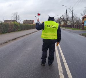 Policjant ruchu drogowego stoi na środku jezdni z uniesioną do góry tarczą do zatrzymywania pojazdów.