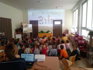 Dzieci siedzą na dywanie, oglądają wyświetlany z projektowa film edukacyjny &#039;Bezpieczne zachowania&quot;