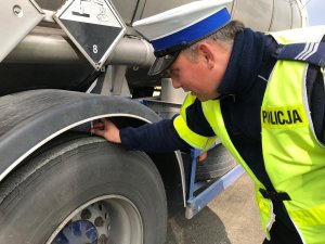 Policjant ruchu drogowego sprawdza wysokość bieżnika opony przy pojeździe ciężarowym.