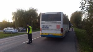 Tył autobusu, na drodze stoi policjant. Z lewej strony na poboczu drogi widoczny zaparkowany radiowóz.