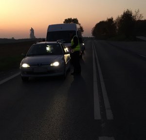 Policjant stoi na środku drogi. Z lewej stron najeżdżają samochody.