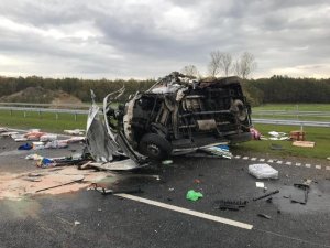 Miejsce wypadku drogowego. Na fotografii widoczny rozbity samochód osobowy koloru białego. Wokół rozrzucone części samochodowe. Droga posypana specjalnym proszkiem w miejscu, gdzie doszło do wycieku płynów eksploatacyjnych.