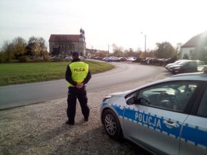 Policjant obserwuje ruch drogowy w rejonie kościoła i cmentarza.