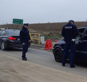 Policjanci ruchu drogowego pełniący służbę przy wykorzystaniu wideorejestratora podczas przeprowadzanej kontroli drogowej. jeden z funkcjonariuszy legitymuje kierującego. Drugi policjant asekuruje.