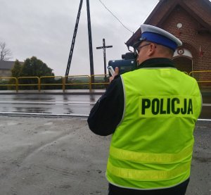 Policjant ruchu drogowego przy użyciu laserowego miernika prędkości wykonuje pomiar.