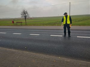 Policjant trzymając w ręku tarczę do zatrzymywania pojazdów wskazuje miejsce do zatrzymania.