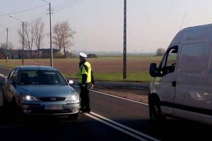 Policjant ruchu drogowego stoi na środku jezdni. Wykonywał sprawdzenie stanu trzeźwości kierowcy samochodu osobowego.