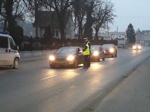 Policjanci ruchu drogowego kontroluj trzeźwość kierowców. Z lewej strony widać nadjeżdżające pojazdy. # z nich stoją oczekując policyjnej kontroli.