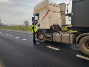 Policjant podczas działań kontroluje kierowcę samochodu ciężarowego przy użyciu alkomatu.