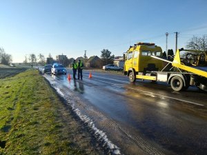 Policjanci podczas oględzin. Funkcjonariusze stroją na jezdni. Za nimi widoczny radiowóz. Z prawej strony autolaweta, która zabiera jeden z uszkodzonych pojazdów.