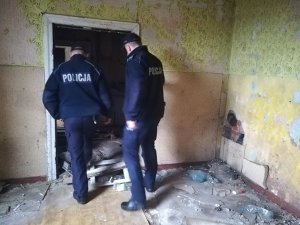 Policjanci w pustostanie. Sprawdzają czy w środku znajdują się jakieś osoby. Wnętrze pomieszczenia nosi ślady zaniedbania.