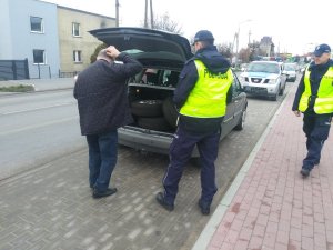 Patrol podczas kontroli drogowej. Jeden z policjantów sprawdza obowiązkowe wyposażenie bagażu. Drugi asystuje.