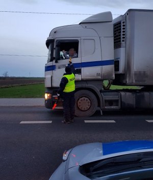 Policjant sprawdza trzeźwość kierowcy samochodu ciężarowego. na pierwszym planie widoczna część radiowozu policyjnego.