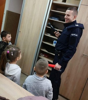 Policjant pokazuje sprzęt wykorzystywany w codziennej służbie. Prezentuje służbową latarkę, która dzięki specjalnej czerwonej nakładce pozwala na zatrzymywanie pojazdów w nocy i jest widoczna z dużej odległości.