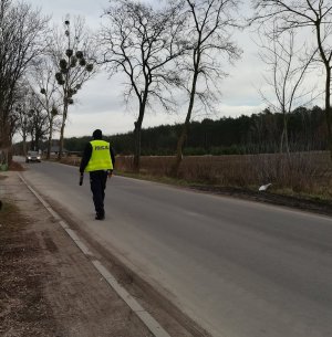 Policjant ruchu drogowego idzie po jezdni. W oddali nadjeżdżający samochód osobowy, którego kierujący przekroczył dozwoloną prędkość.