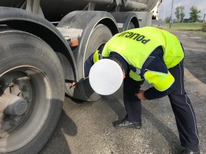 Policjant ruchu drogowego kontroluje stan ogumienia pojazdu ciężarowego