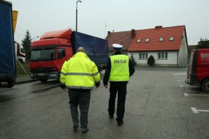 Kierujący i funkcjonariusz policji na parkingu, idą w kierunku zaparkowanego pojazdu ciężarowego.