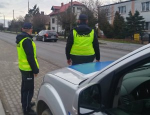 Umundurowani policjanci stoją przy radiowozie, na poboczu drogi