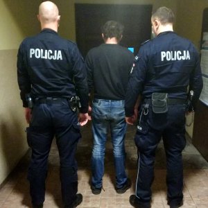 Umundurowani policjanci stoją z zatrzymanym mężczyzną