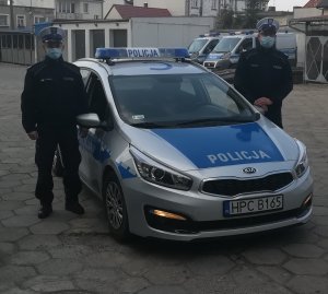 Na zdjęciu jest dwóch policjantów stojących przy radiowozie