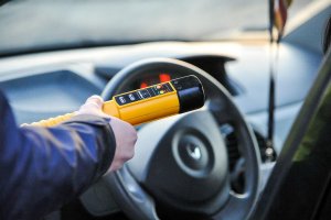 stojący przy samochodzie  policjant  trzyma  w ręku alcoblow