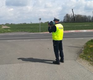 obrazek przedstawia policjanta, który miernikiem prędkości mierzy prędkość pojazdu