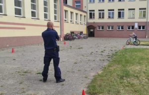 Na obrazku widoczny jest policjant egzaminujący na kartę rowerową ucznia jadącego rowerem