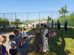 Obrazek przedstawia policjanta oraz dzieci na boisku szkolnym