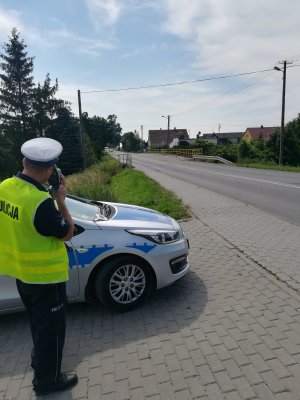 Zdjęcie przedstawia policjanta, który mierzy prędkość miernikiem prędkosci