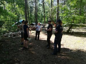 na terenie  obozowiska w lesie policjanta, dwóch strażaków, Komendanci obozowiska rozmawiają  o bezpiecznym przebiegu wypoczynku