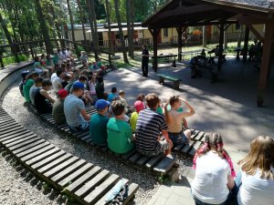 grupa dzieci zajmuje miejsce na terenie amfiteatru rozmawiają z umundurowaną policjantką