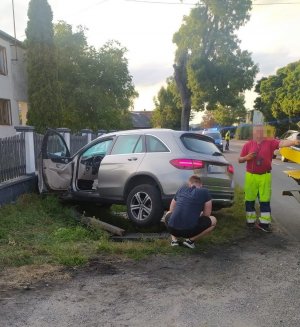 dwie  osoby znajdują się przy uszkodzonym w skutek zdarzenia drogowego pojeździe  marki Mercedes