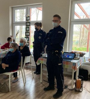 mł. asp. Dariusz Świwiński i sierż. szt. Katarzyna Leszczyńska - Krawczyk podczas prelekcji. Z lewej strony widoczne stoły, przy których siedzą seniorzy.