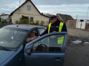 Policjant ruchu drogowego żnińskiej komendy podczas czynności kontrolnych. Z lewej strony w samochodzie marki Opel siedzi starszy mężczyzn.