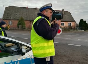 Policjant przy pomocy laserowego miernika prędkość sprawdza, z jaką prędkością poruszają się samochody.