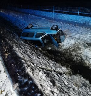 Fotografia przedstawia uszkodzony samochód marki Citroen, który leży na boku w rowie. Jest ciemno.  Wokół leży śnieg.