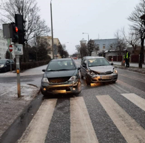 Uszkodzone w wyniku kolizji, Toyota i Citroen stoją przed przejściem dla  pieszych, policjant kieruje  ruchem