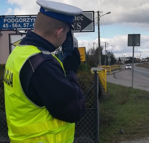 policjant  ruchu drogowego dokonuje  pomiaru prędkości za  pomocą ręcznego miernika  prędkości