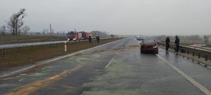 Widok na drogę S5. Z lewej strony dwa pasy jezdni oddzielone terenem zielonym od dwóch pasów znajdujących się po prawej stronie. Z prawej strony fotografii pojazd marki Mercedes z uszkodzeniami po kolizyjnymi. Jezdnia posypana specjalnym preparatem przez Strażaków  W oddali samochód Straży Pożarnej.