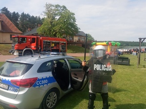 chłopiec ubrany w  strój policjanta stoi przy oznakowanym radiowozie