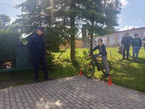 przed torem egzaminacyjnym na  kartę rowerową stoi chłopak z rowerem, policjant i przyglądający się chłopcy