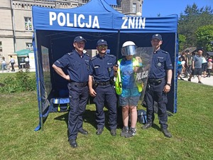 Trzech policjantów i chłopiec ubrany w policyjny sprzęt na tle namiotu policyjnego.