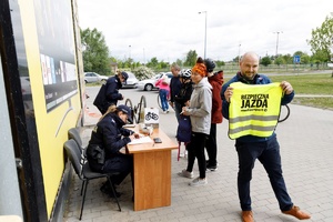 Mężczyzna, który trzyma w rękach żółtą kamizelkę odblaskową z napisem bezpieczna jazda z Media Expert. W tle stoisko znakowania rowerów.