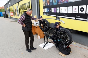 Policjantka znakuje rower. Z drugiej strony pojazdu stoi jego właściciel i przytrzymuje koło. W tle stoisko do znakowania rowerów.