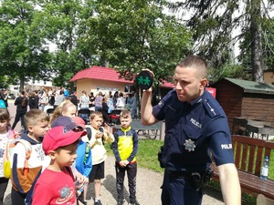 Młodszy aspirant Michał Tylak dzielnicowy pokazuje dzieciom zasadę użytkowania tuby profilaktycznej. Zachęca przy tym do korzystania z odblasków.